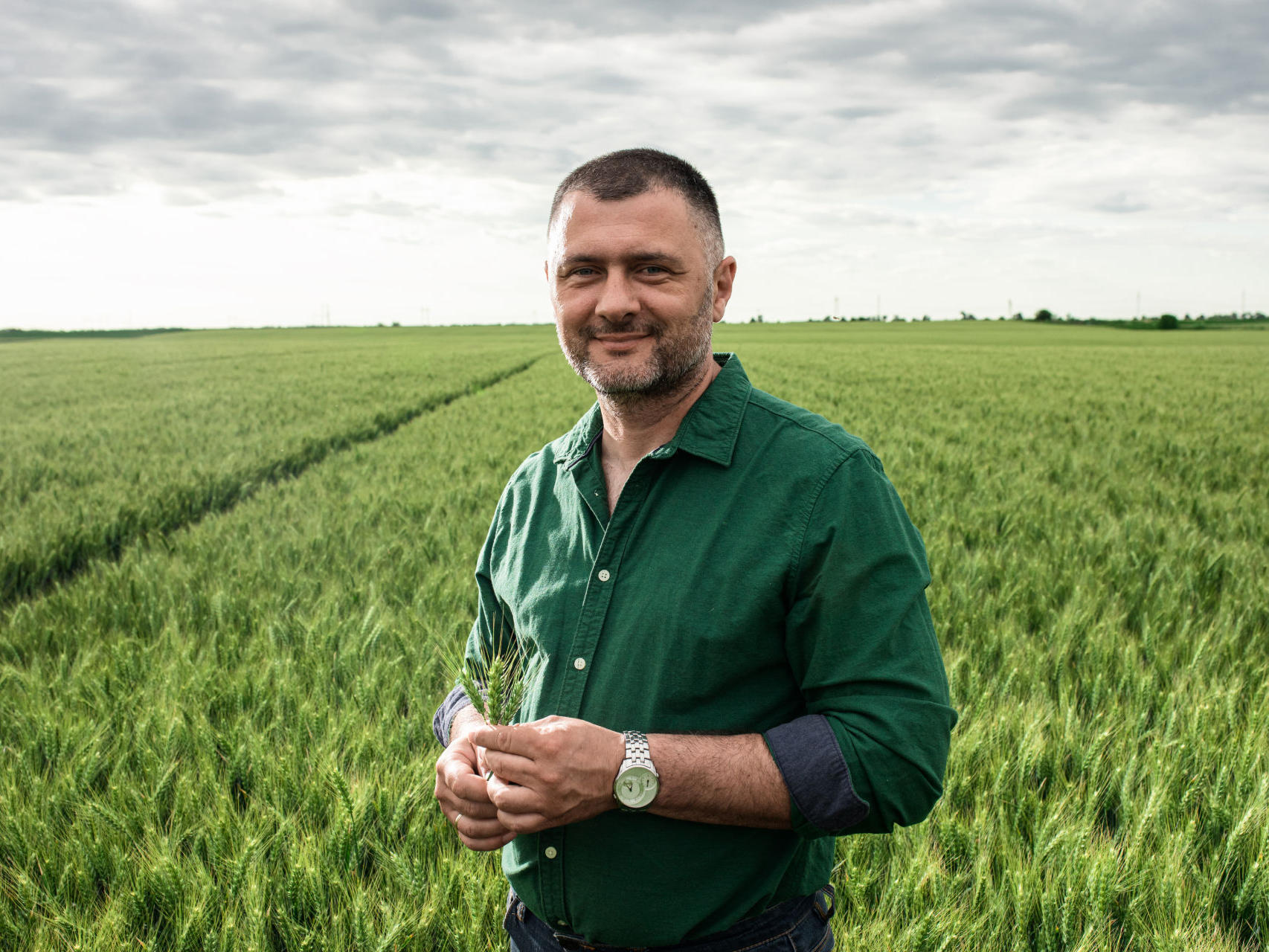 Rolnik stojący przed swoim polem, trzymający kłos zboża w ręce