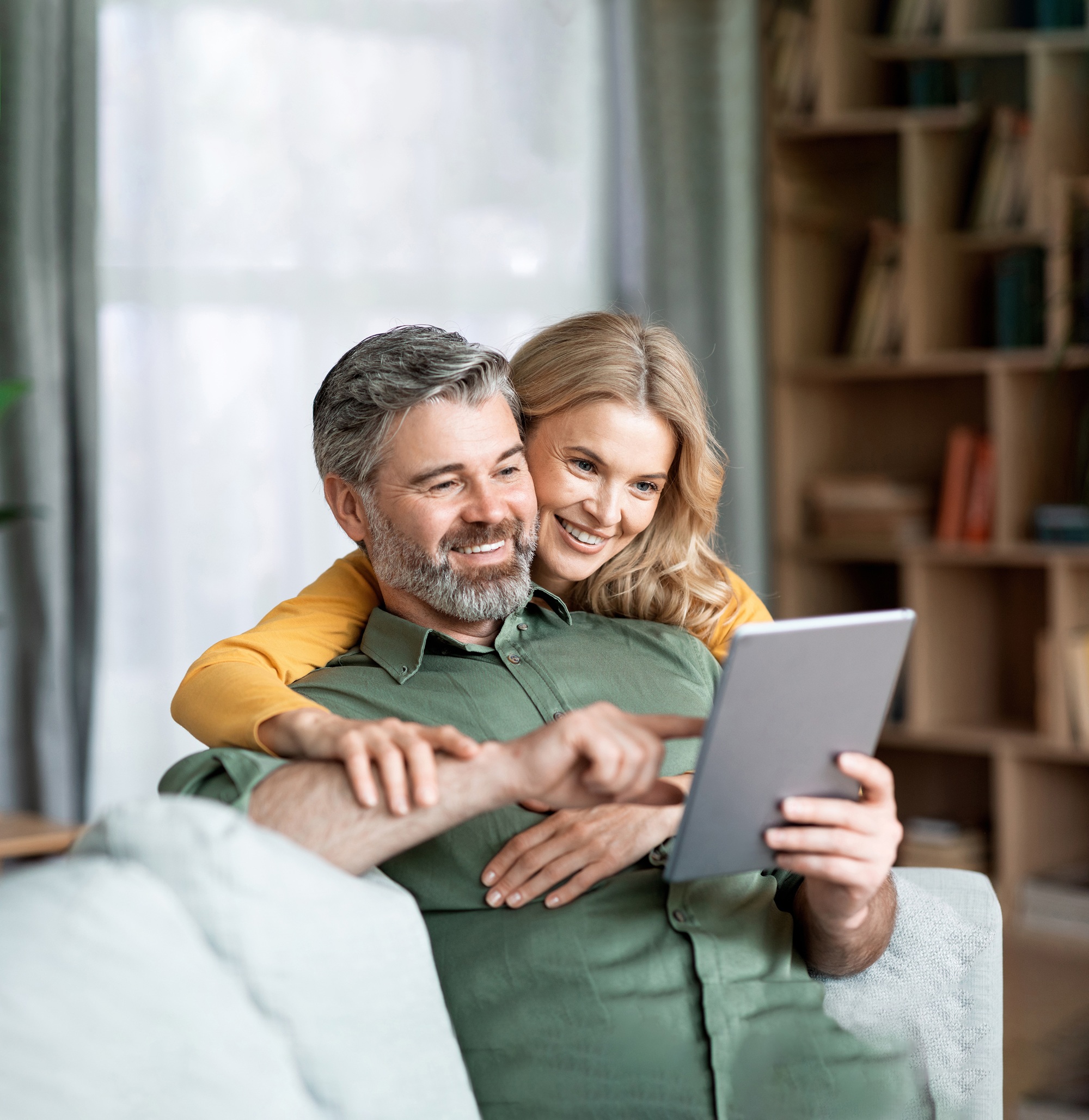 Uśmiechnięci mężczyzna i kobieta siedzą na kanapie wpatrując się w tablet