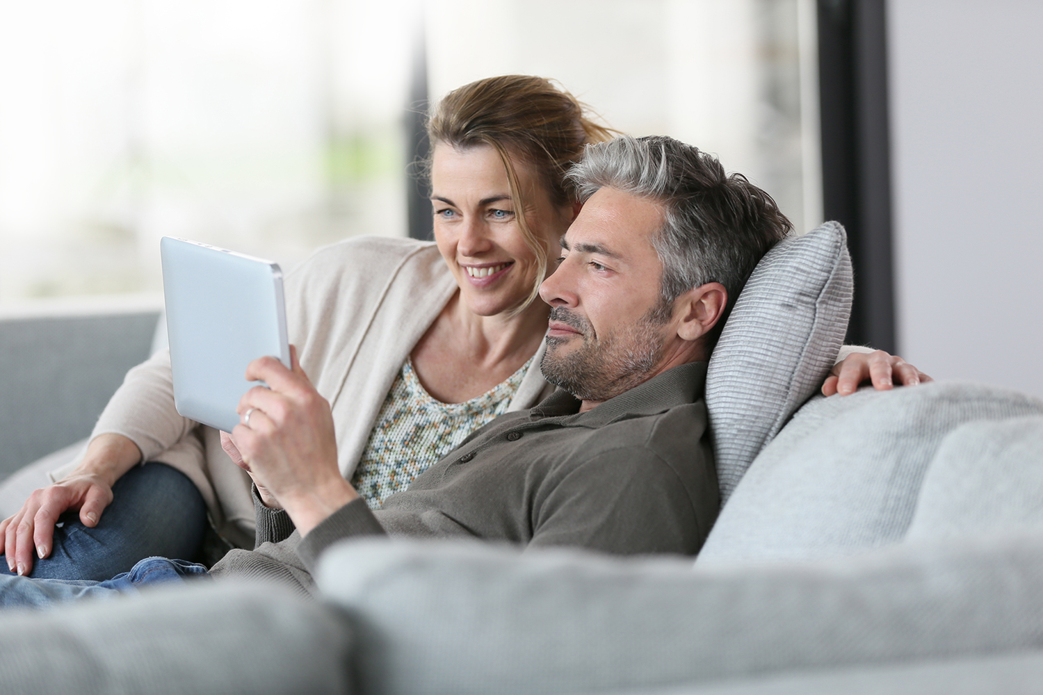 Mężczyzna i kobieta leżą na kanapie wpatrując się w tablet, kobieta się uśmiecha
