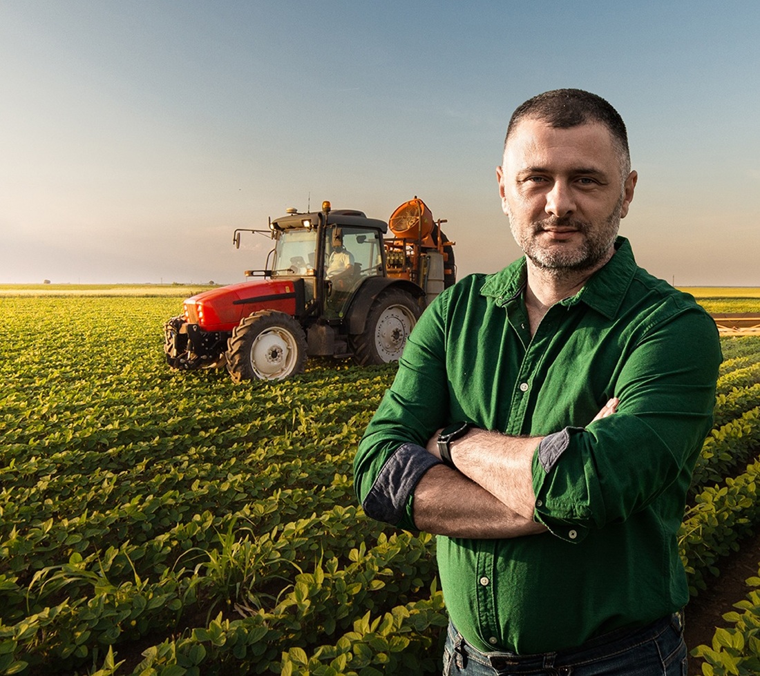 Rolnik stojący przed swoim polem, za nim na polu traktorzysta w traktorze